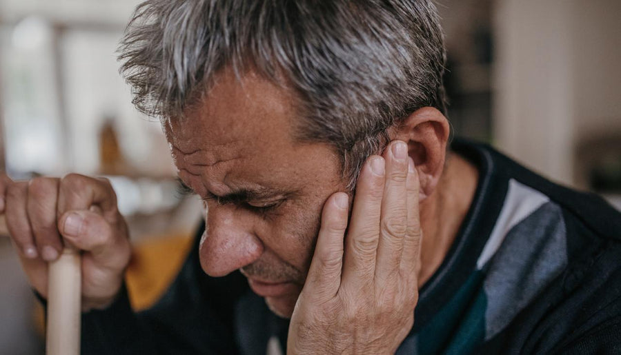 Middle-aged man presses hand to ear in pain, holding cane, experiencing earache indoors