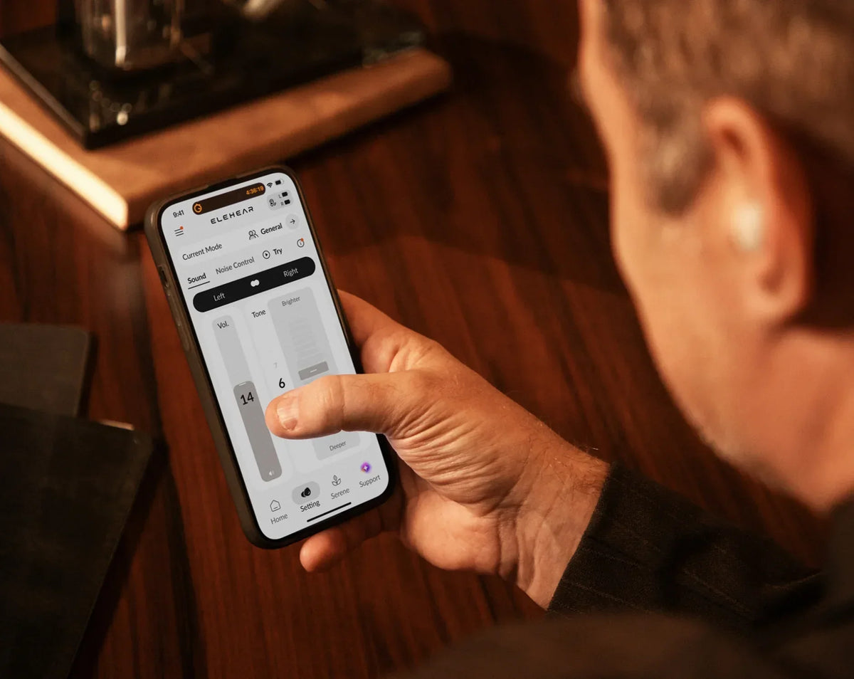 Older adult adjusting hearing settings on a smartphone with a hearing aid.