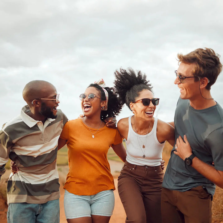 Group of friends laughing outdoors, man wearing Elehear hearing aid enjoying social gathering