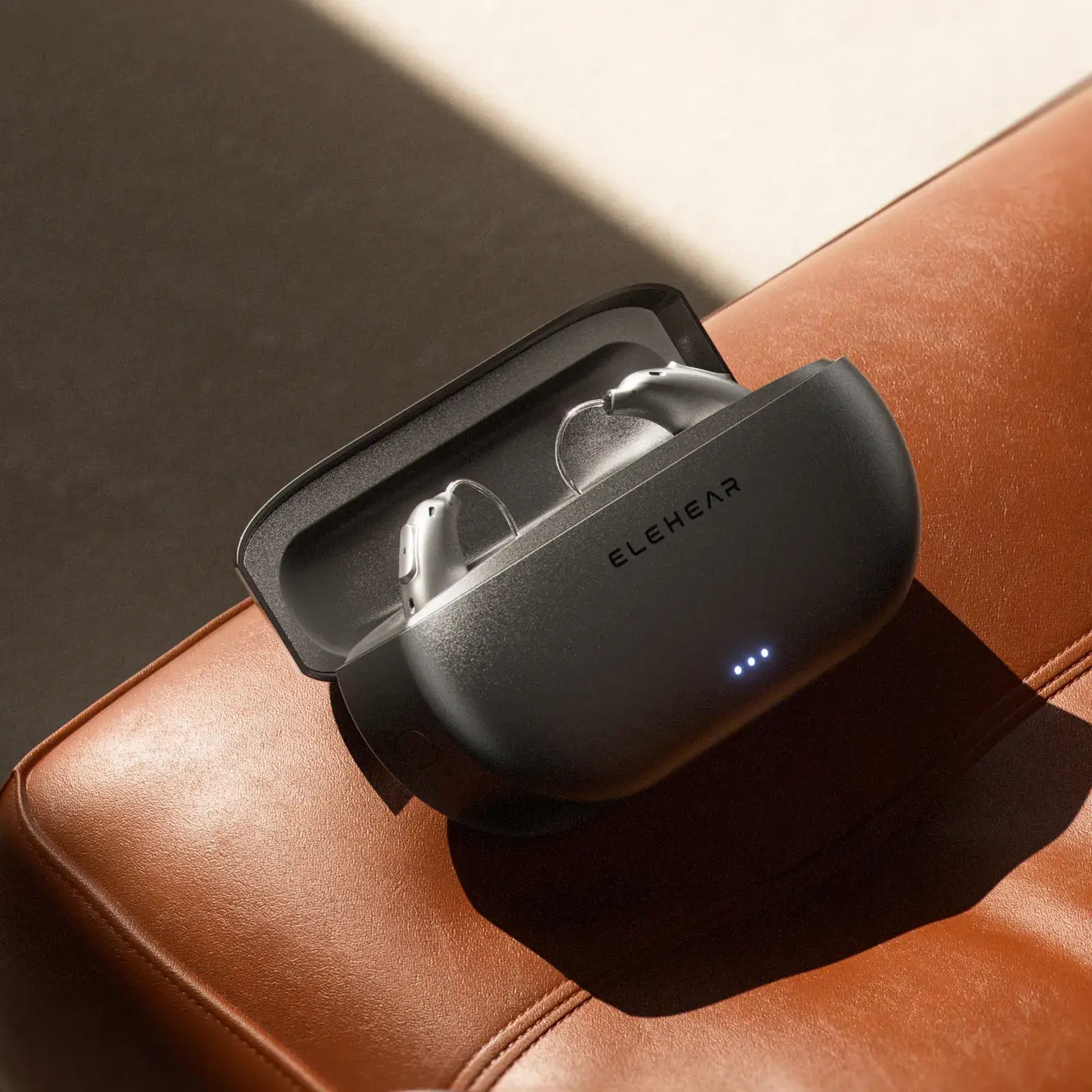 ELEHEAR Beyond Pro silver hearing aids in open charging case on tan leather surface with LED indicators