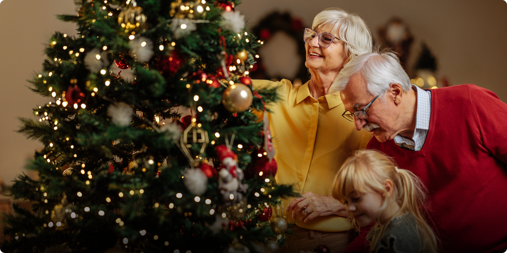 Senior couple with a young girl in front of a decorated Christmas tree.