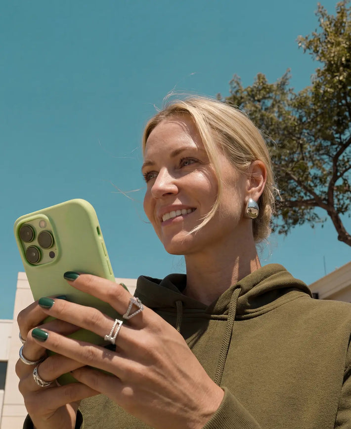 Woman holding a green phone outdoors with a clear blue sky and tree in the background