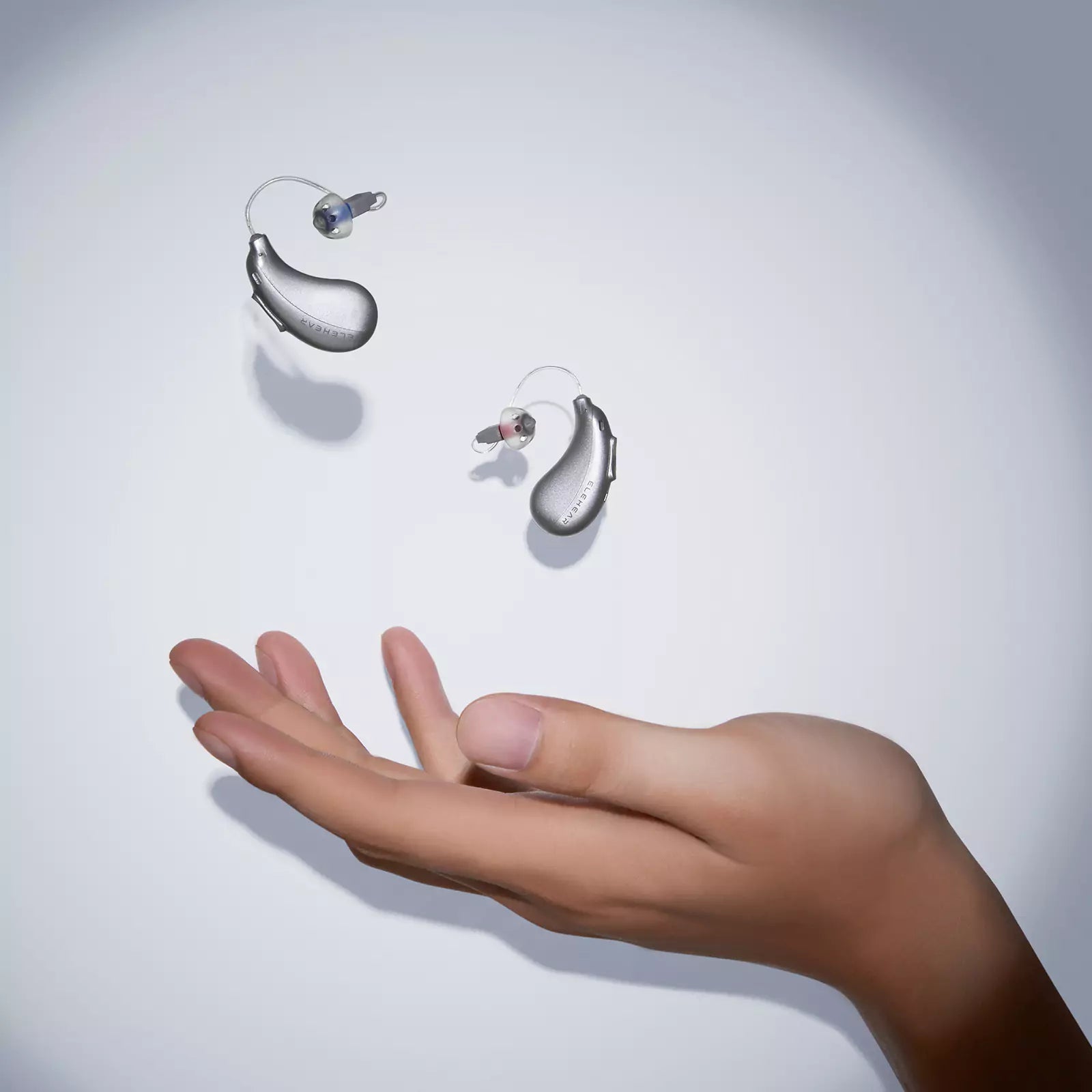 Hand reaching toward lightweight behind-the-ear hearing aids floating in air showing ergonomic design and portability