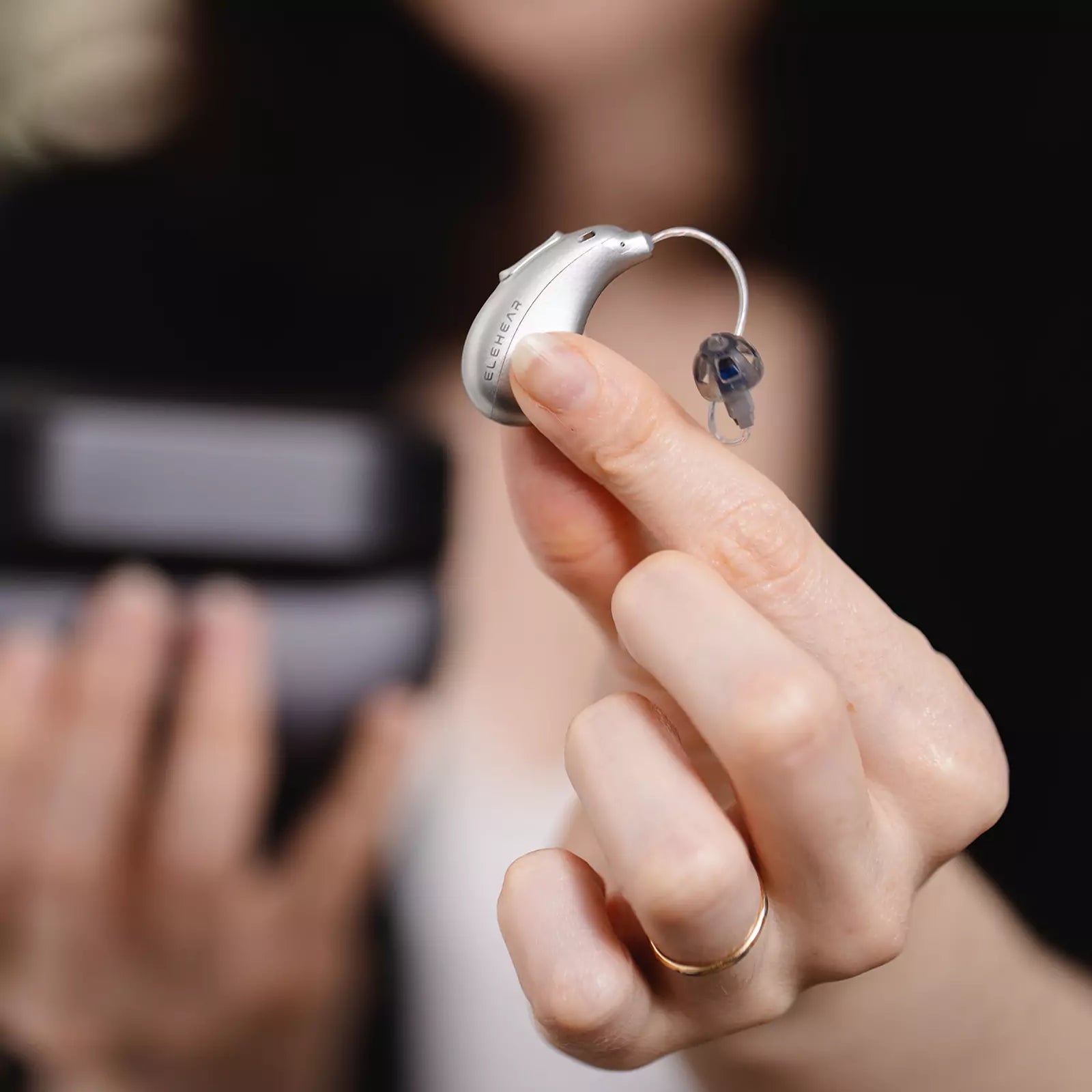 Woman holding small discreet behind-the-ear hearing aid showing compact size and comfortable fit