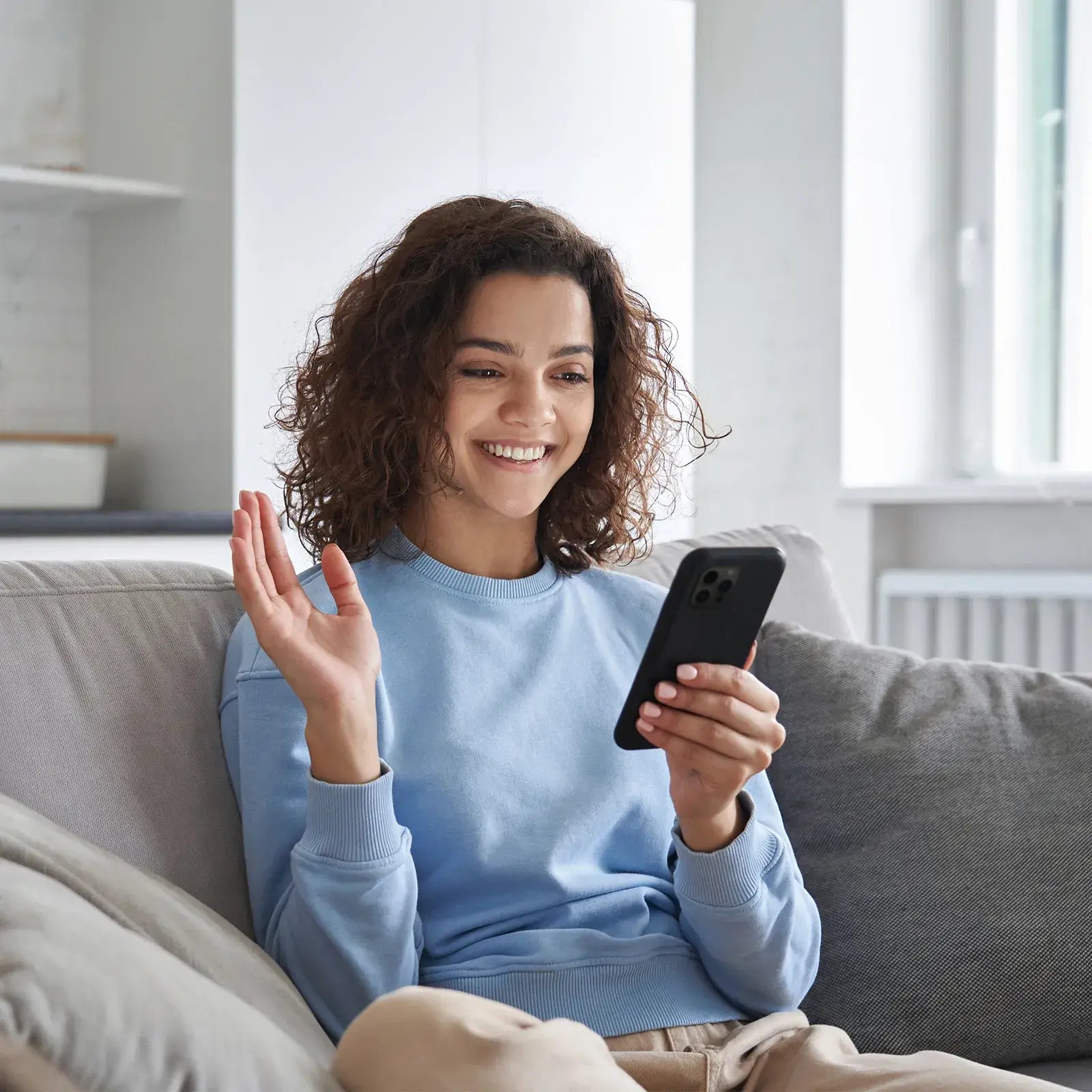 Woman waving during video call on smartphone while wearing hearing aids for clear communication